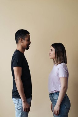 Karışık ırk çiftleri birbirlerine bej arka planda bakarlar.