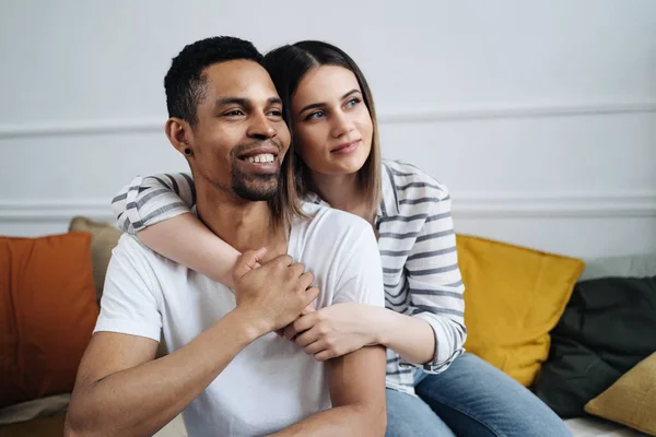 Front view of young diverse couple sitting on a couch at home — Stock Photo, Image