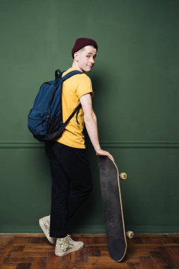 Sarı tişörtlü beyaz adam koyu yeşil arka plan duvarında paten yapıyor.