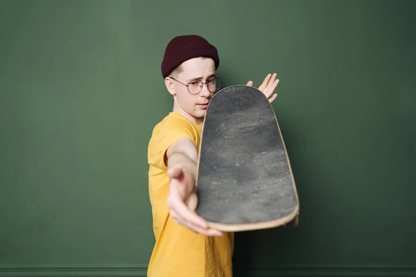 Hombre caucásico en camiseta amarilla posando con patín sobre pared de fondo verde oscuro — Foto de Stock