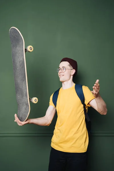 Fehér férfi sárga pólóban pózol korcsolyával át sötét zöld háttér fal — Stock Fotó