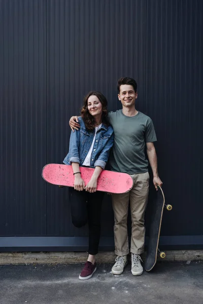 Moderni hymyilevä pari seisoo yhdessä rullalaudat — kuvapankkivalokuva