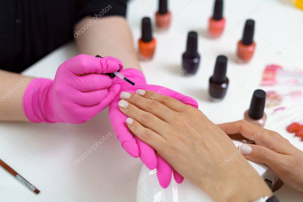 Manicurist treating client at beauty nails salon. Manicure, painting on nail