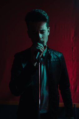 Deri ceketli bir adam kulüpte karanlık bir sahnede gösteri yapıyor.