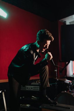 Deri ceketli bir adam otantik bir stüdyoda karanlık bir yerde şarkı söylüyor.