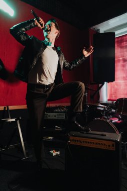 Deri ceketli bir adam otantik bir stüdyoda karanlık bir yerde şarkı söylüyor.