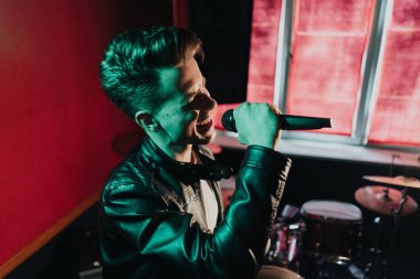 Deri ceketli bir adam kulüpte karanlık bir sahnede gösteri yapıyor.