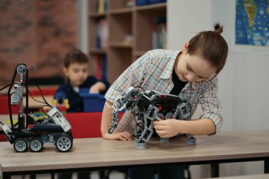 İki farklı yaşta çocuk okul robotları sınıfında robot oyuncaklarla oynuyor.