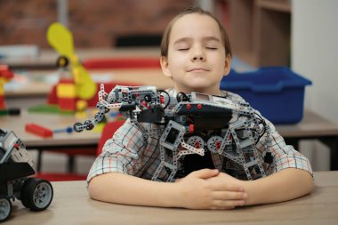 Akıllı okul çocuğu masada oturuyor ve robot bir cihaz yapıyor.