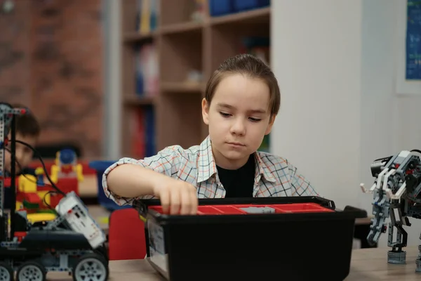 Chytrý školák sedí u stolu a staví robotické zařízení — Stock fotografie