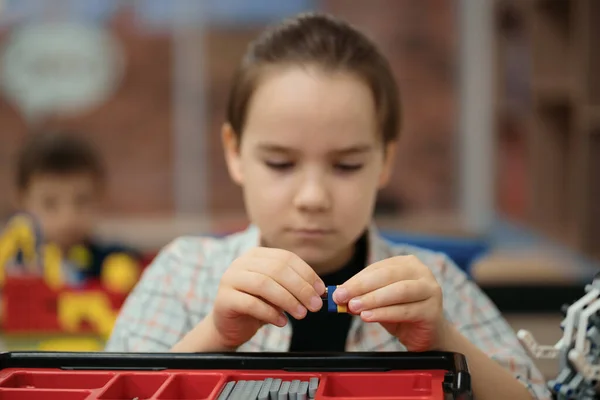 Smart schoolboy sitting at the table and constructing a robotic device