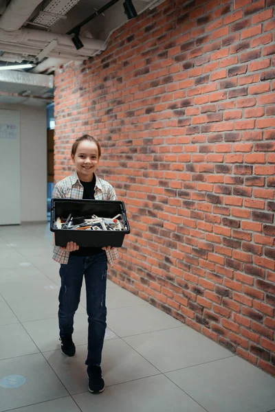 Niño caminando mientras sostiene una caja de paz robótica en el fondo de la pared de ladrillo — Foto de Stock