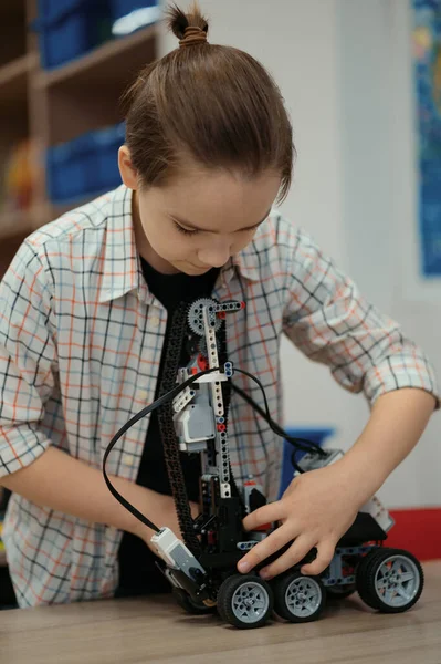 Akıllı okul çocuğu masada oturuyor ve robot bir cihaz yapıyor. — Stok fotoğraf