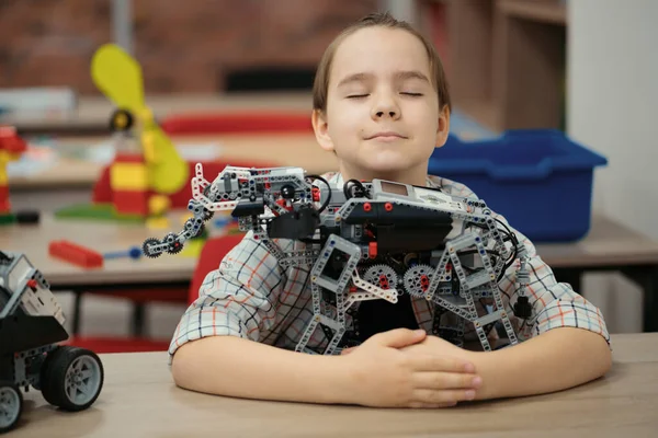 Smart schoolboy sitting at the table and constructing a robotic device