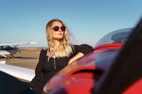 Preciosa dama en gafas de sol posando cerca de avión —  Fotos de Stock