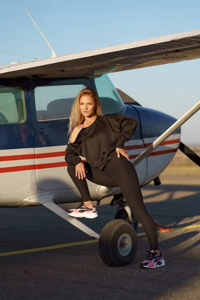 Model poseren in sport outfit bij een vliegtuig — Stockfoto