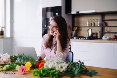 Genç çiçekçi dizüstü bilgisayara bakıyor ve telefona cevap veriyor.