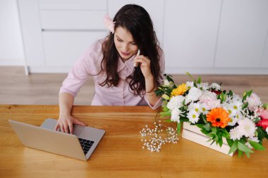 Genç çiçekçi dizüstü bilgisayara bakıyor ve telefona cevap veriyor.