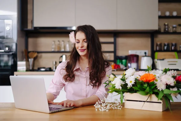 Portret van het werken potige brunette met bloemen en laptop aan tafel — Stockfoto