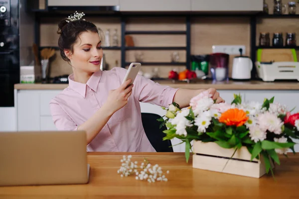 Fiatal virágárus laptopot néz és telefonál. — Stock Fotó