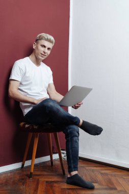 Burgonya duvarının yanındaki sandalyede oturan dizüstü bilgisayarlı genç adam.
