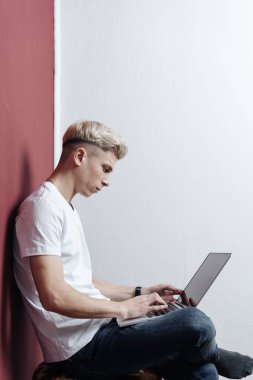 Burgonya duvarının yanındaki sandalyede oturan dizüstü bilgisayarlı genç adam.