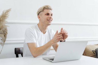 Gülümseyen adam beyaz bir alanda bilgisayar kullanarak çalışıyor.