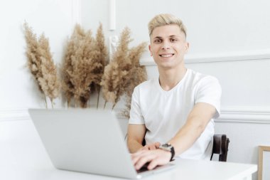 Gülümseyen adam beyaz bir alanda bilgisayar kullanarak çalışıyor.