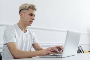 Gülümseyen adam beyaz bir alanda bilgisayar kullanarak çalışıyor.