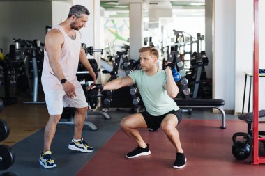 Genç adam spor salonunda kişisel antrenörle antrenman yapıyor.