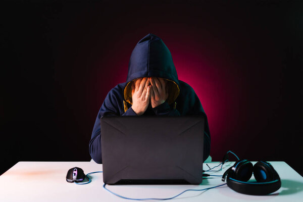 Professional hacker with laptop sitting at table on dark background