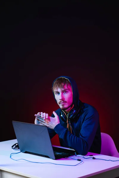 Hacker profissional com laptop sentado à mesa no fundo escuro — Fotografia de Stock