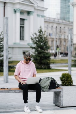 Sokakta bir bankta otururken bilgisayarını kullanan afro bir adam.