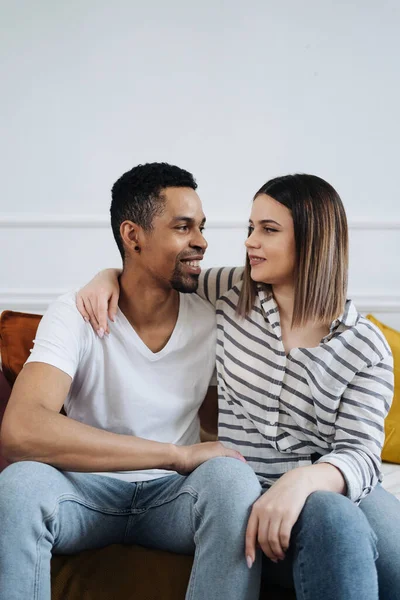 Front view of young diverse couple sitting on a couch at home — Stock Photo, Image