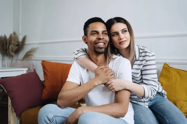 Front view of young diverse couple sitting on a couch at home — Stock Photo, Image