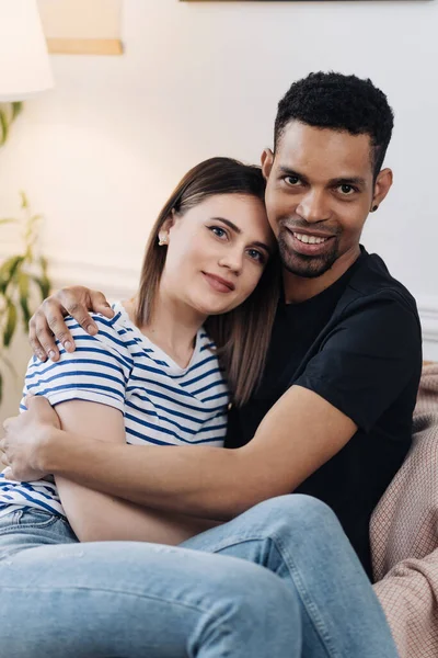 Vue de face du jeune couple diversifié assis sur un fauteuil à la maison — Photo