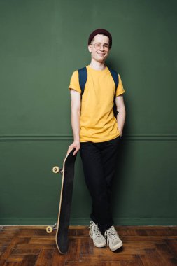 Sarı tişörtlü beyaz adam koyu yeşil arka plan duvarında paten yapıyor.