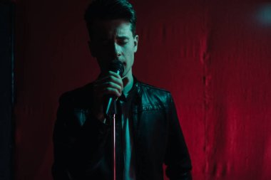 Deri ceketli bir adam kulüpte karanlık bir sahnede gösteri yapıyor.