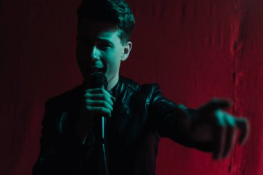 Deri ceketli bir adam kulüpte karanlık bir sahnede gösteri yapıyor.