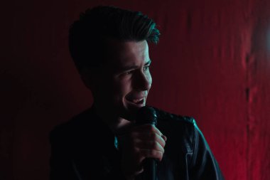 Deri ceketli bir adam kulüpte karanlık bir sahnede gösteri yapıyor.