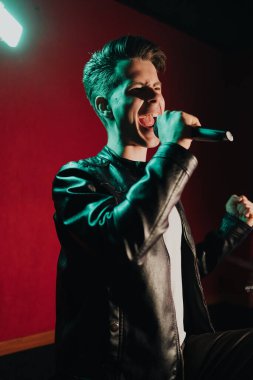 Deri ceketli bir adam kulüpte karanlık bir sahnede gösteri yapıyor.
