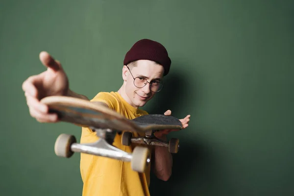 Hombre caucásico en camiseta amarilla posando con patín sobre pared de fondo verde oscuro — Foto de Stock