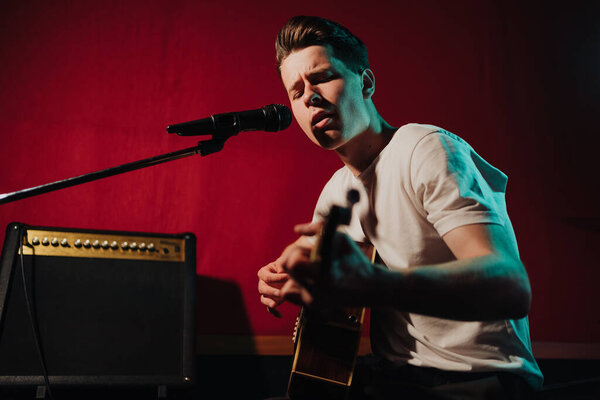 Young male hipster recording new sounds at studio while playing electro guitar and singing