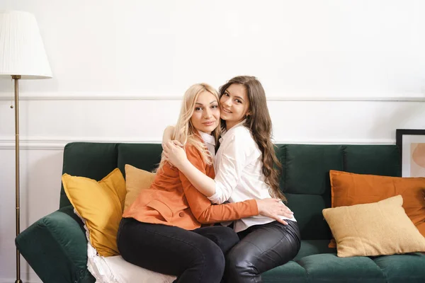 Hermosa mamá y su hija adulta están abrazando y sonriendo mientras están sentados en el sofá en casa —  Fotos de Stock