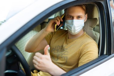 Genç bir erkek, tıbbi bir maske takmış ve cep telefonu kullanıyor.