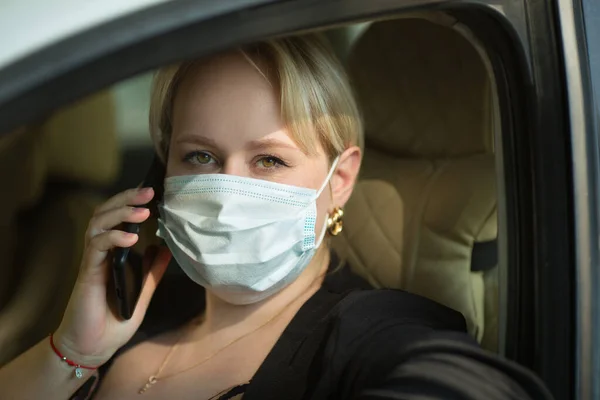 携帯電話のある医療用マスクで車を運転する美しい若い太っ腹な女性 — ストック写真