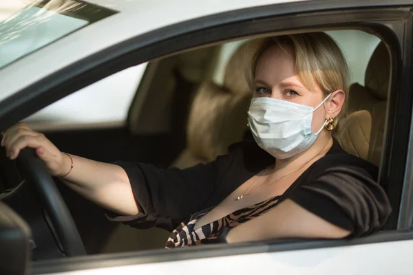 美しい若い豊満な女性が医療マスクをした車を運転し — ストック写真