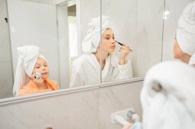 Güzel anne ve kızı banyoda aynanın yanında bornozlu.