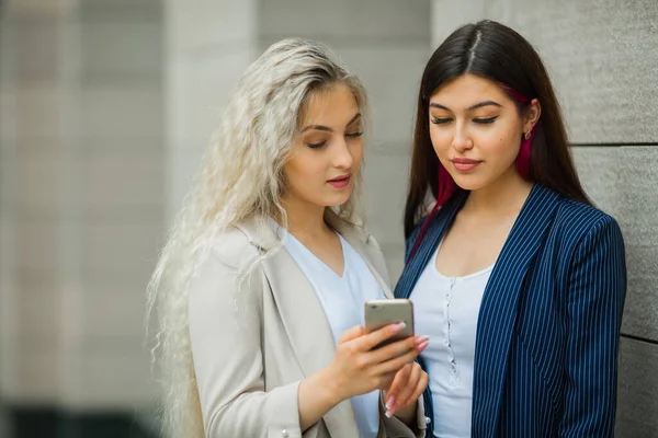 two beautiful young women in suits with a mobile phone