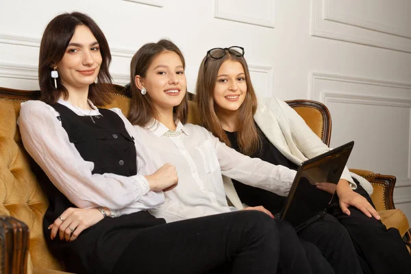three young women on the couch at the laptop